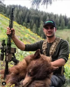 man holding an ar15 rifle in right hand while displaying a bear in the left.