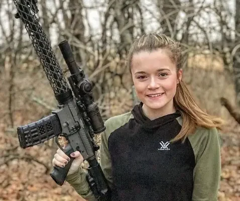 female smiling and holding an ar15 rifle with carbon fiber handguard.