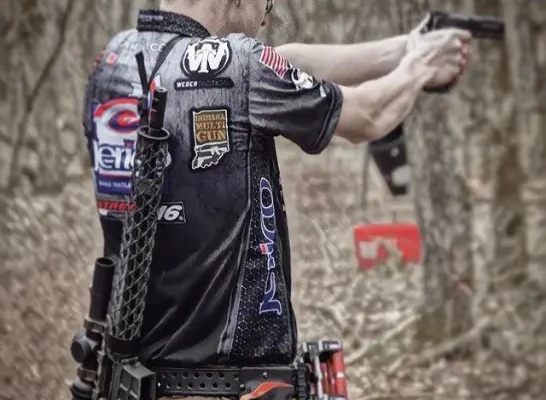 3 gun competitor shooting his pistol with his lightweight ar15 stored on his back.
