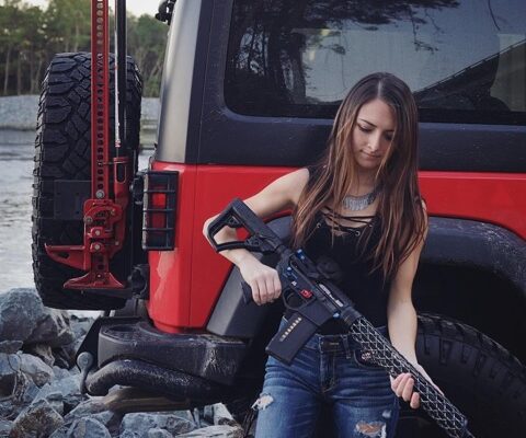 Girl holding an AR15 with carbon fiber handguard leaning against a red jeep.